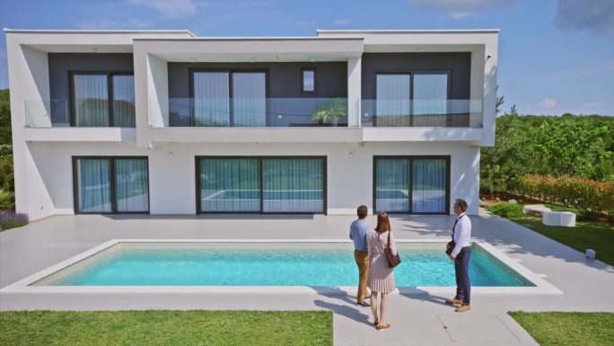 CS男房地产经纪人向一对站在泳池边的已婚夫妇展示一栋现代化的房子