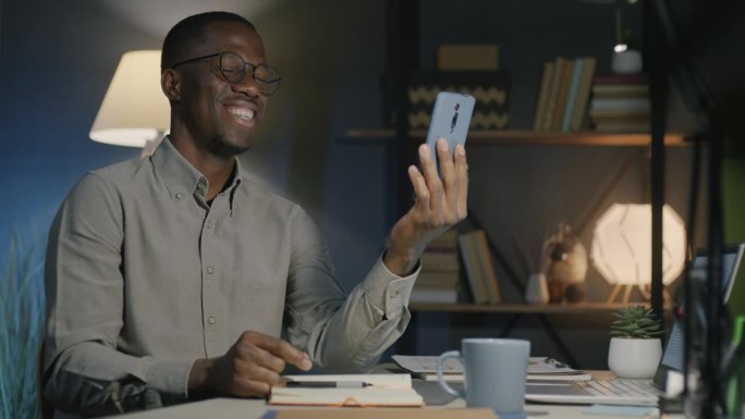 非裔美国男性企业家在漆黑的办公室里用智能手机聊天工具进行在线视频通话