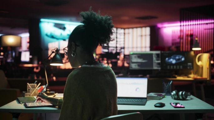 背景:晚上在创意公司使用笔记本电脑和平板电脑的黑人女性，经理正在为客户执行商业策略。专家撰写项目计划