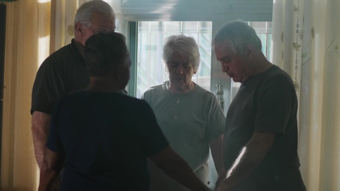四位老人在家祷告，一群坦诚的老人朋友站在窗户旁，在阳光的照射下进行祷告和奉献