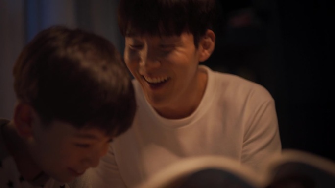 韩国父亲在睡觉前给他可爱的儿子读童话故事。耐心的父亲帮助儿子学习如何阅读他最喜欢的书。亲子亲密时刻