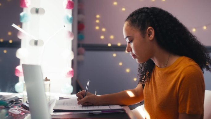 十几岁的女孩在家里的卧室里用笔记本电脑学习