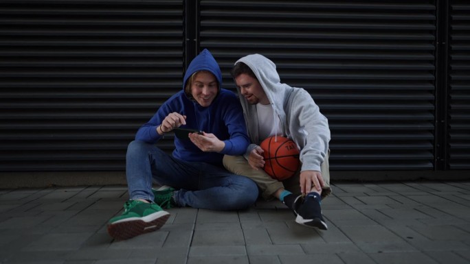 一名患有唐氏综合症的男子和他的朋友在户外打篮球时休息。友谊的概念和残疾人融入社会。