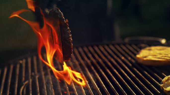 商业风格的超级慢动作镜头与一个匿名厨师翻转汉堡肉在火焰烧烤。一个美味的牛肉饼的特写正在餐馆里烹饪