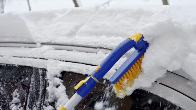 在一个下雪的早晨，用刷子清理她车上的积雪。冬季准备的概念，日常事务和照顾自己的车辆