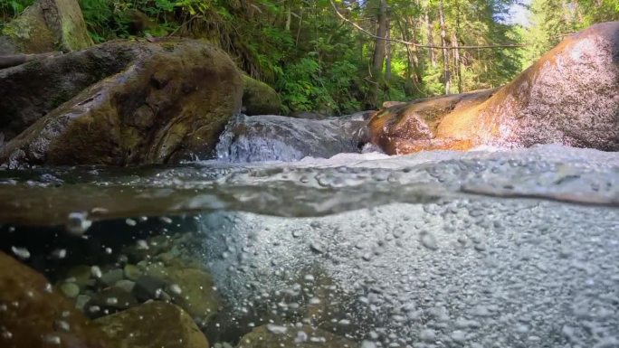 热带雨林中有一条清澈的河流。半水下的慢动作拍摄的溪流之间的石头与小瀑布。纯净的水和泡泡在丛林河