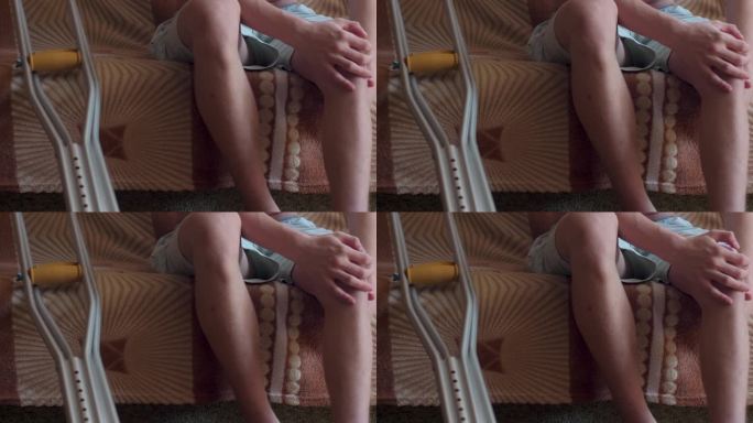 一个拄着拐杖坐在沙发上的年轻人抓住了一条疼痛的腿。腿部受伤后的恢复。保险和医药。事故