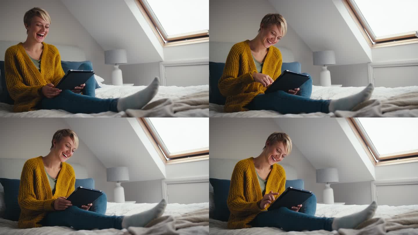 年轻女子坐在家里的床上笑着看着数码平板电脑
