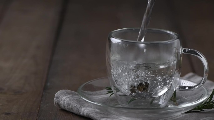 在木桌上煮热茶。将水壶里的开水倒入装有干茶的杯子里。木桌上的透明茶杯是刚泡好的茶