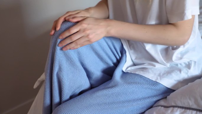 一名穿着睡衣的妇女在清早起床后按摩她疼痛的膝盖