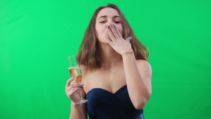 醉醺醺的年轻女子拿着香槟酒杯看着镜头跳舞，做着飞吻的手势。醉醺醺的白人女士在派对上的肖像，在绿幕背景