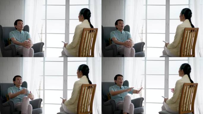 亚洲男性在咨询室与女性心理医生交谈，成熟男性在心理治疗室与心理咨询师讨论面临的问题