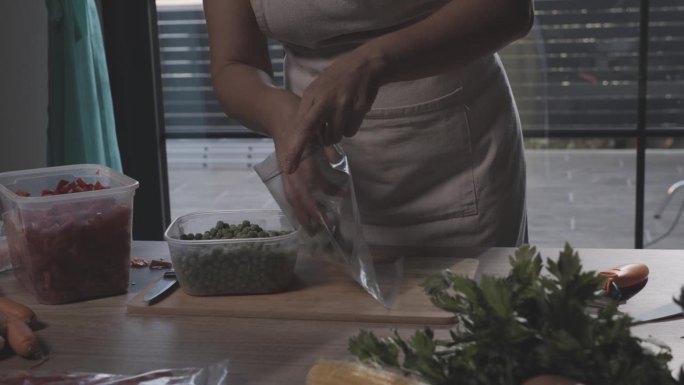 一名妇女在为冬天保存食物时将豌豆放入塑料冷冻袋中