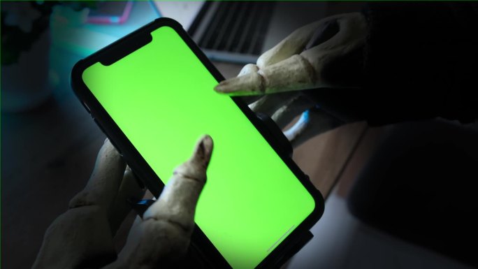 穿着骷髅服的手拿着绿色屏幕的智能手机，在社交网络上滚动