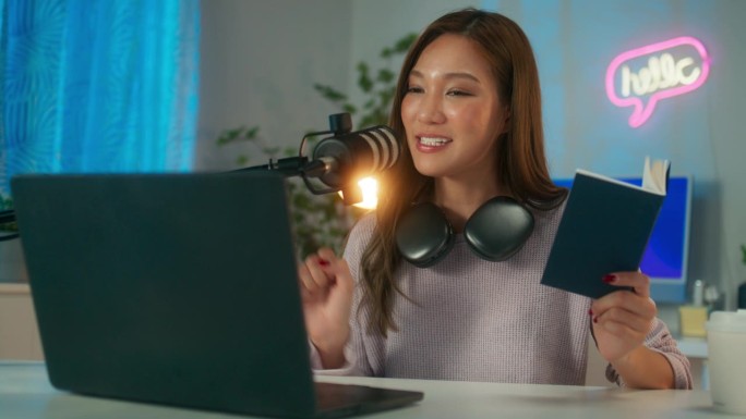 快乐的年轻亚洲女性电台主持人或播客，戴着耳机在麦克风上说话，在家庭工作室里运行播客