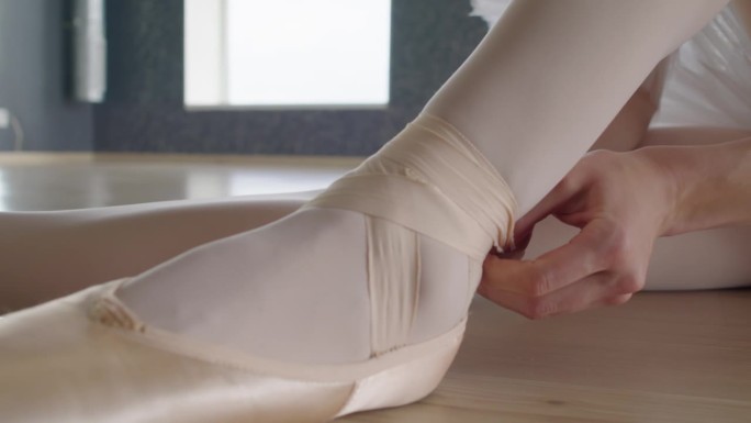 芭蕾舞女演员把缎带系在脚踝上，同时把脚尖放在脚上