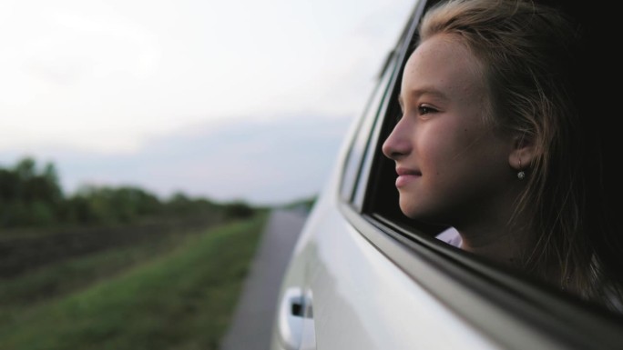 快乐的家庭旅行。小女孩探出车窗挥手。快乐的小女孩把她的手臂伸出开着的车窗外。夏日自驾游概念。