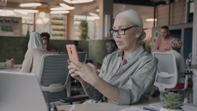 成熟的女商人使用智能手机发短信，在共享办公室享受在线交流