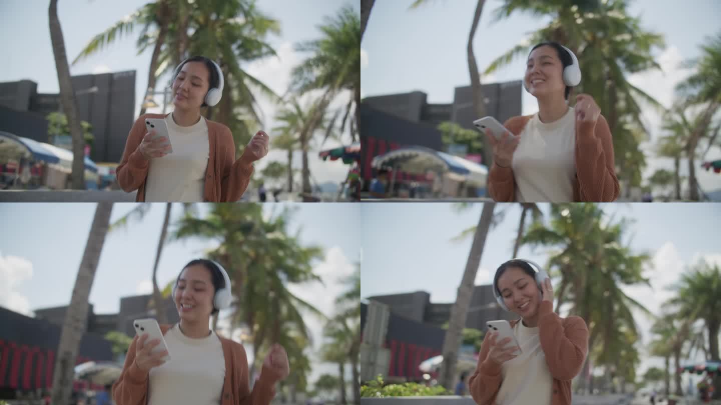 年轻的亚洲女子戴着无线耳机，拿着智能手机在沙滩上跳舞