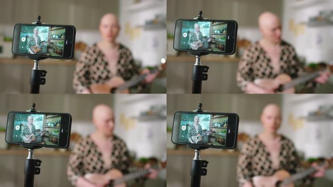 智能手机屏幕上，年轻的秃顶女子一边弹吉他一边流媒体