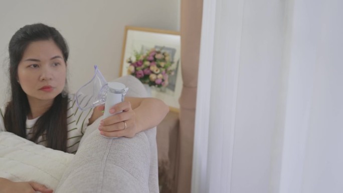 患有哮喘的亚洲妇女住在家里，正在用吸入器和蒸笼照顾自己。