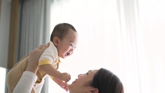 幸福的母子在家里亲吻并将男婴抛向空中