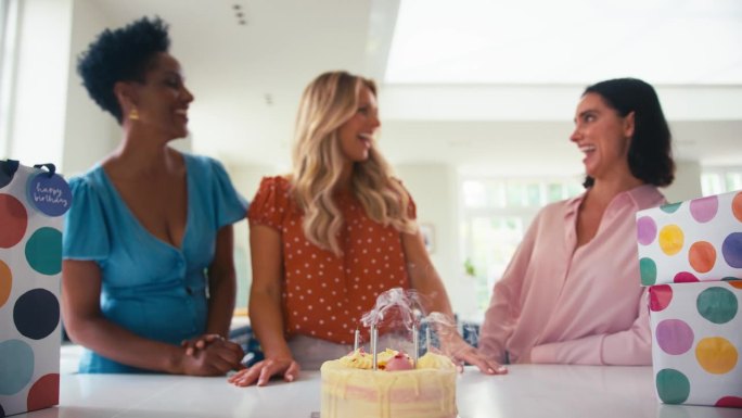 一个成熟的女人在家和朋友一起庆祝生日，吹灭蛋糕上的蜡烛