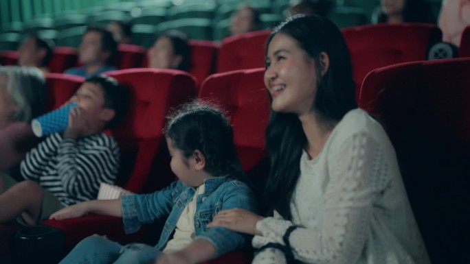 年轻微笑的亚洲母亲带着女儿在电影院看电影…