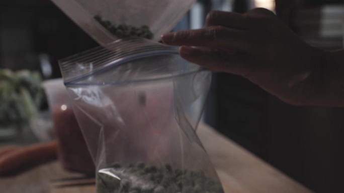 一名妇女在为冬天保存食物时，将豌豆倒入塑料冷冻袋中