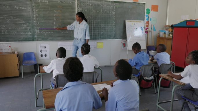 特写平移视图。非洲黑人女教师站在黑板前，在非洲的一间教室里给孩子们上课