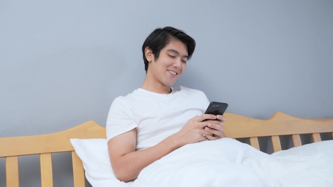 亚洲男子在卧室玩手机。