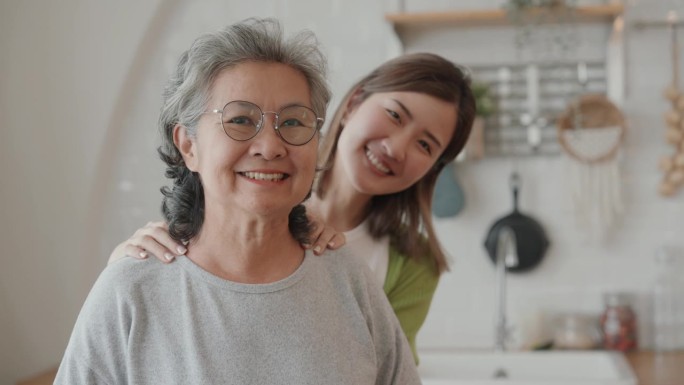 一个微笑的老太太和她的孙女在厨房里的肖像，做饭，看着相机。