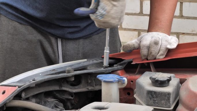 一个男人正在他家院子里的车库附近修理他的汽车。一名男子用扳手拧下螺栓，更换汽车上坏了的部件。汽车修理