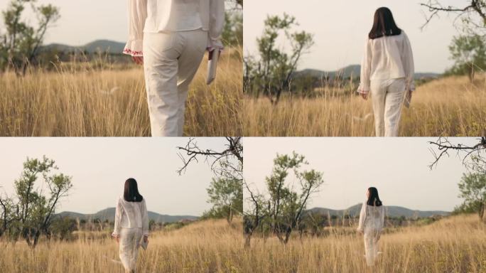夕阳西下，身穿白衣的年轻女子走过一片草地
