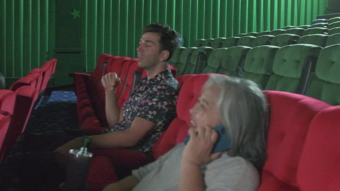 老年妇女在电影院使用手机干扰其他观众。
