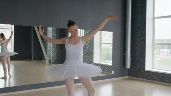 穿着芭蕾舞服的年轻女子在舞蹈室里挥舞着手臂跳舞