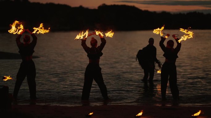 夏夜河滩上的火焰表演，手持火把的年轻女子剪影