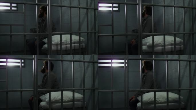 罪犯坐在牢房的床上，望着铁窗