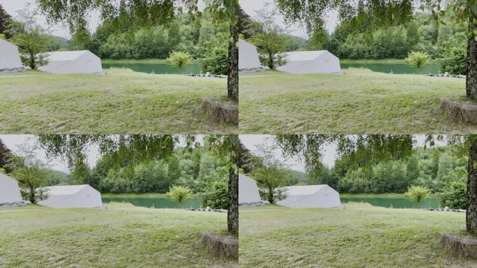 白色的大帐篷在草坪上，有几棵树，背景是森林的湖