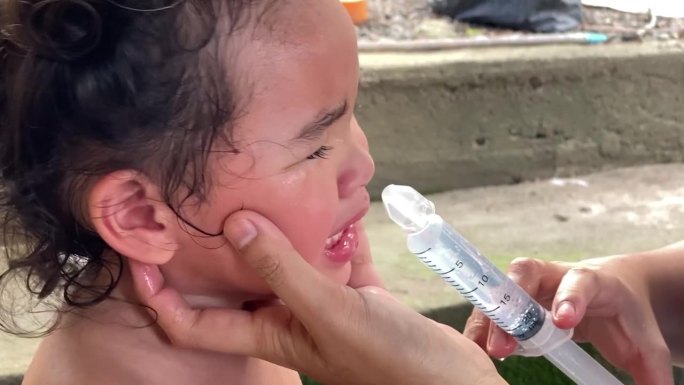 一位亚洲母亲正在帮她的小女儿用盐水冲洗鼻腔