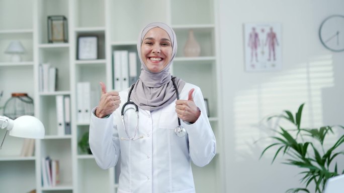 在现代医院的诊所里，快乐的穆斯林女医生站在办公室里竖起大拇指