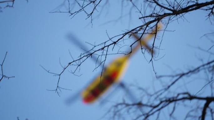 一架散焦的ADAC德国救援直升机在蓝天中飞过树木的跟踪镜头