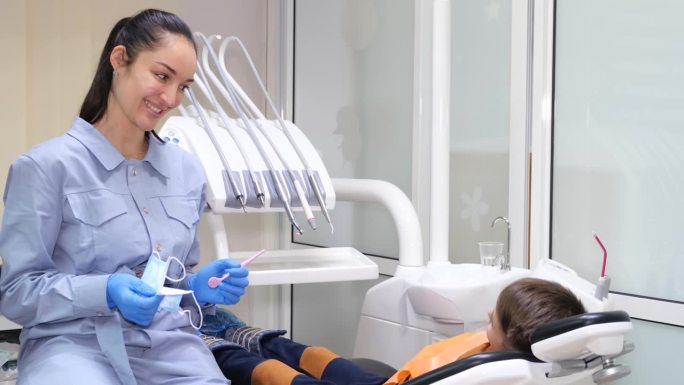 和蔼可亲，微笑的女牙医在给一个小男孩做牙科咨询。