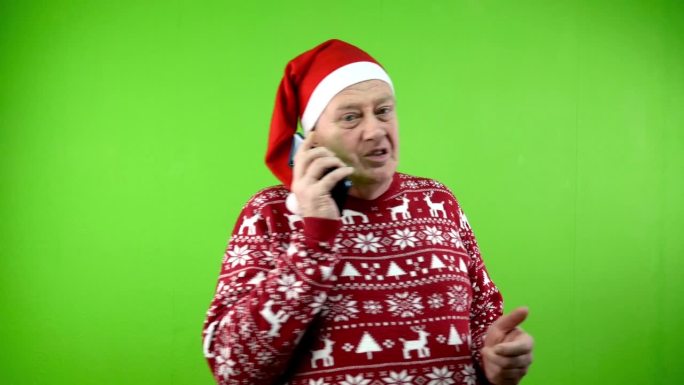 戴红色圣诞帽，穿着圣诞毛衣的老人一边走一边打电话。