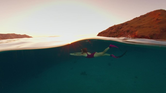 一名身穿粉色潜水服的女子在日落时分畅游在印度尼西亚科莫多国家公园的水下世界