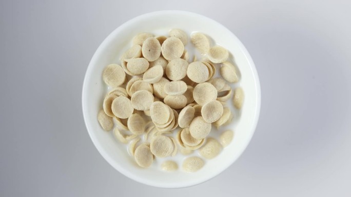 早餐用甜菊糖在白色碗与牛奶，俯视图。早餐麦片，干的拼成贝壳状的脆片。4K视频，旋转