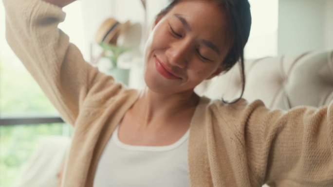特写亚洲女孩穿着白色的奶油色睡衣，在舒适的床上快乐地跳舞，在家里的卧室里度过了漫长的假期。女性早晨的
