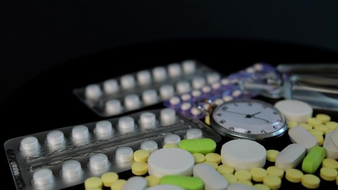 药品和药品在黑色的桌子上旋转。药品、药片、水疱、安瓿和怀表