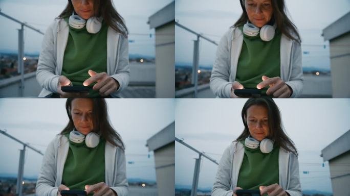戴耳机的女子在城市屋顶上使用智能手机