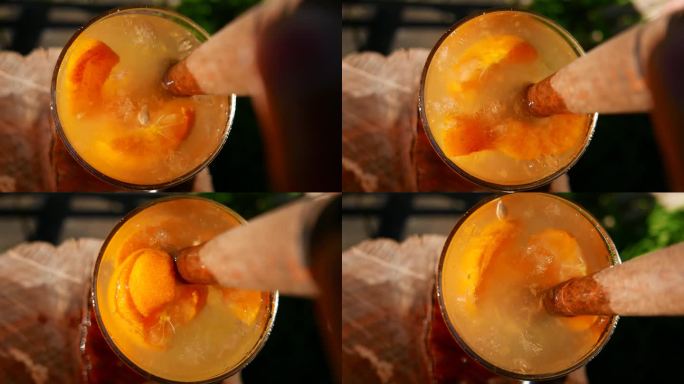 POV:一个人在调制橘色凯匹林纳酒的特写镜头。桌上有巴西凯匹林纳酒。搅拌凯皮林纳鸡尾酒。使用木制搅拌